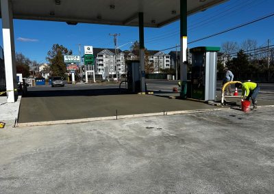 A gas station under construction with a cemented area and a worker wearing a neon vest.