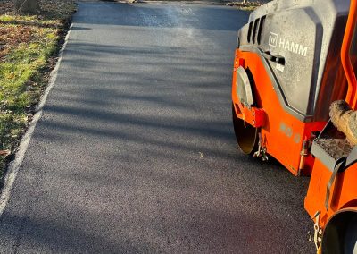 Freshly paved driveway with a steamroller and worker smoothing the asphalt.