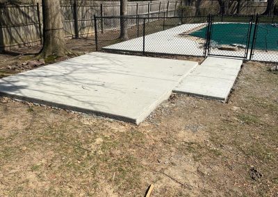 Concrete slabs next to a fenced-in, tarp-covered pool in a backyard with trees and grass.