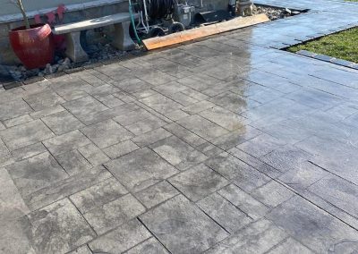 Wet stone patio with a hose and gardening tools near a bench; grassy yard in the background.