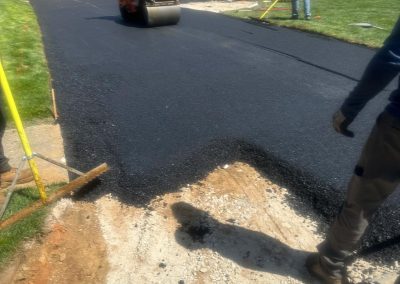 Workers repaving a driveway with fresh asphalt in front of a suburban house.