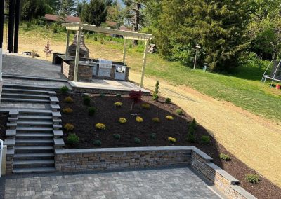 Terraced backyard with patio, landscaped garden, outdoor kitchen, and grassy area.
