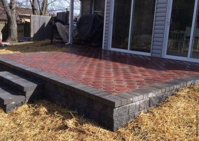Brick patio with three steps, next to a house with sliding glass doors and surrounded by straw-covered ground.