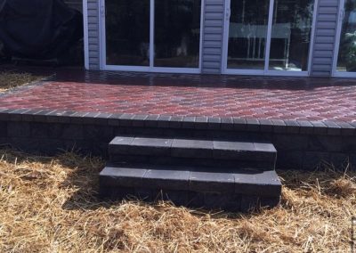 Brick patio with two steps leading to a sliding glass door, surrounded by straw-covered ground.
