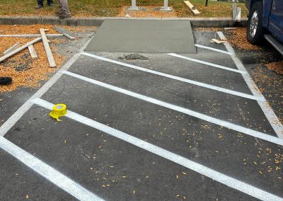 Two workers near a freshly poured concrete patch by mailboxes, surrounded by construction materials.