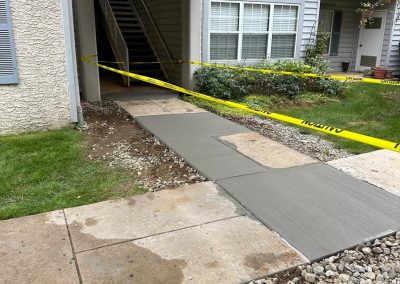 Freshly poured concrete walkway with caution tape near an apartment building's stairway.