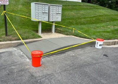 Freshly poured concrete sidewalk section blocked off with caution tape and orange buckets in a residential area.