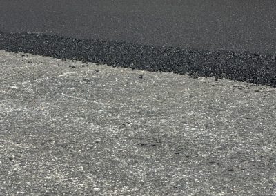 Person paving road with asphalt near a metal building and red ladder.