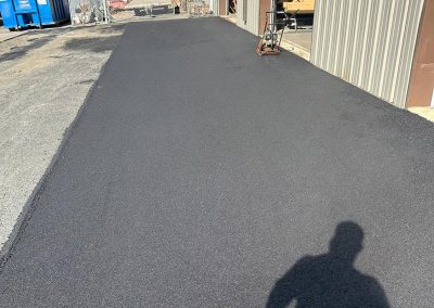 Freshly paved asphalt path beside a building, with a person's shadow in the foreground.
