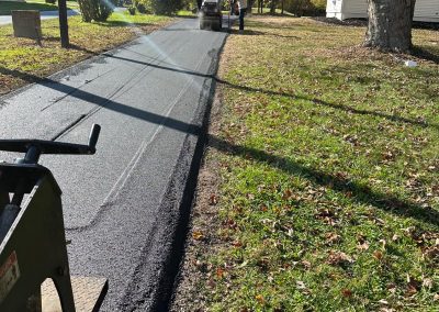 Workers paving a road surrounded by trees and houses on a sunny day.