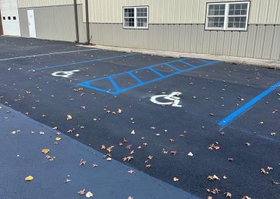 Parking lot with handicapped spaces marked in blue near a beige building, scattered with fallen leaves.