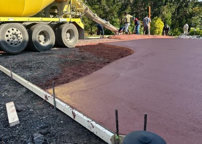 Concrete mixer pouring onto a driveway, with workers in the background and trees lining the scene.