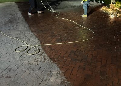 Two people cleaning a brick driveway with a hose at night.