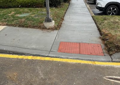 Sidewalk with tactile paving next to parked cars and apartment buildings; overcast sky.