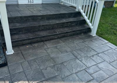 Gray stone steps and porch with white railing leading to a white house door, surrounded by green grass.