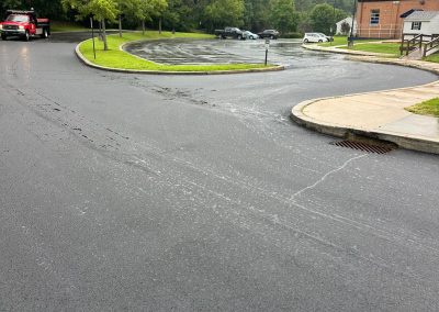Wet asphalt parking lot with a few cars and trees. Overcast sky and a corner building visible.