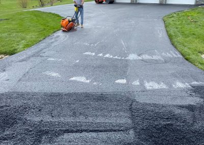 Person paving driveway with asphalt near a garage and grassy lawn.