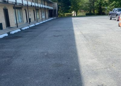A two-story motel with a parking lot, surrounded by trees under a clear blue sky.