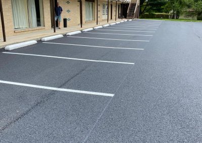 Empty parking lot in front of a brick building with a person standing by a door.