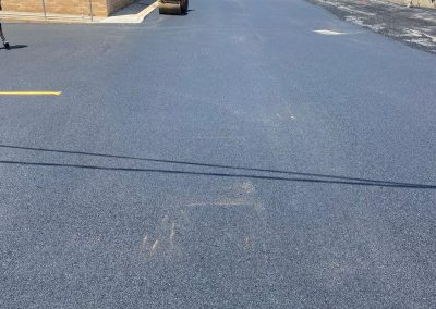 Freshly paved asphalt road with surrounding houses and clear skies.