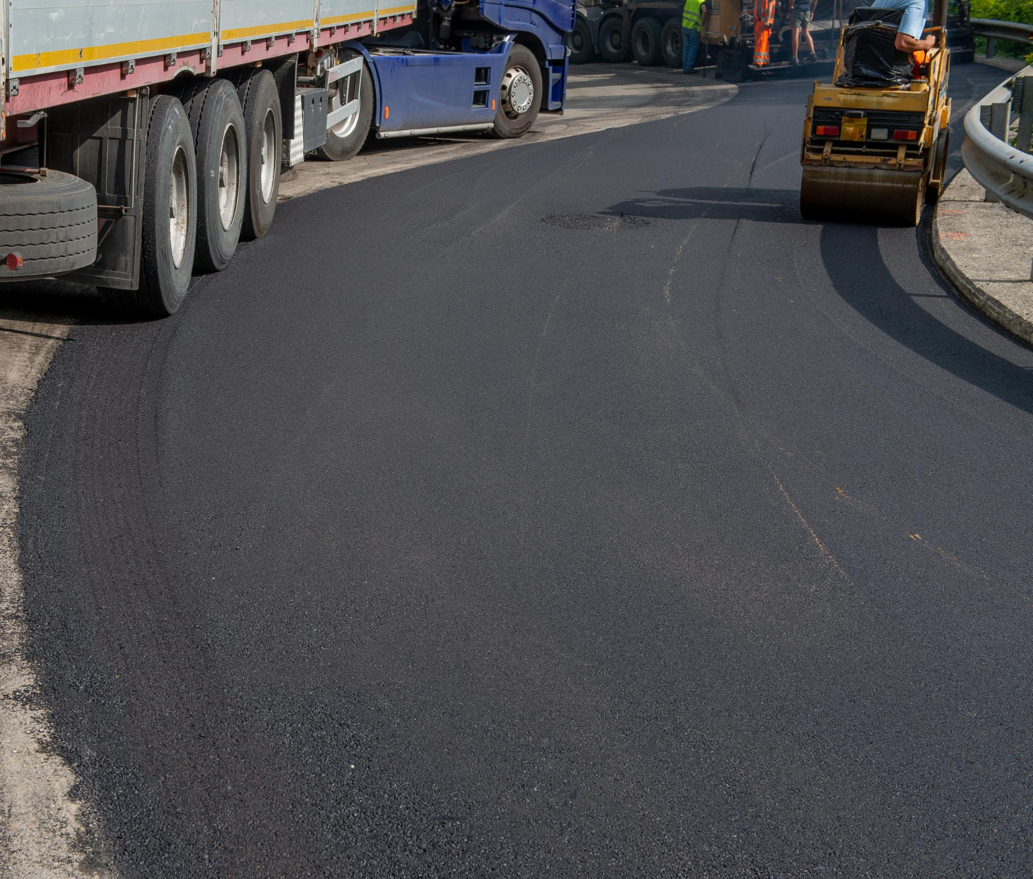 Freshly paved road with construction vehicles and workers visible in the background.